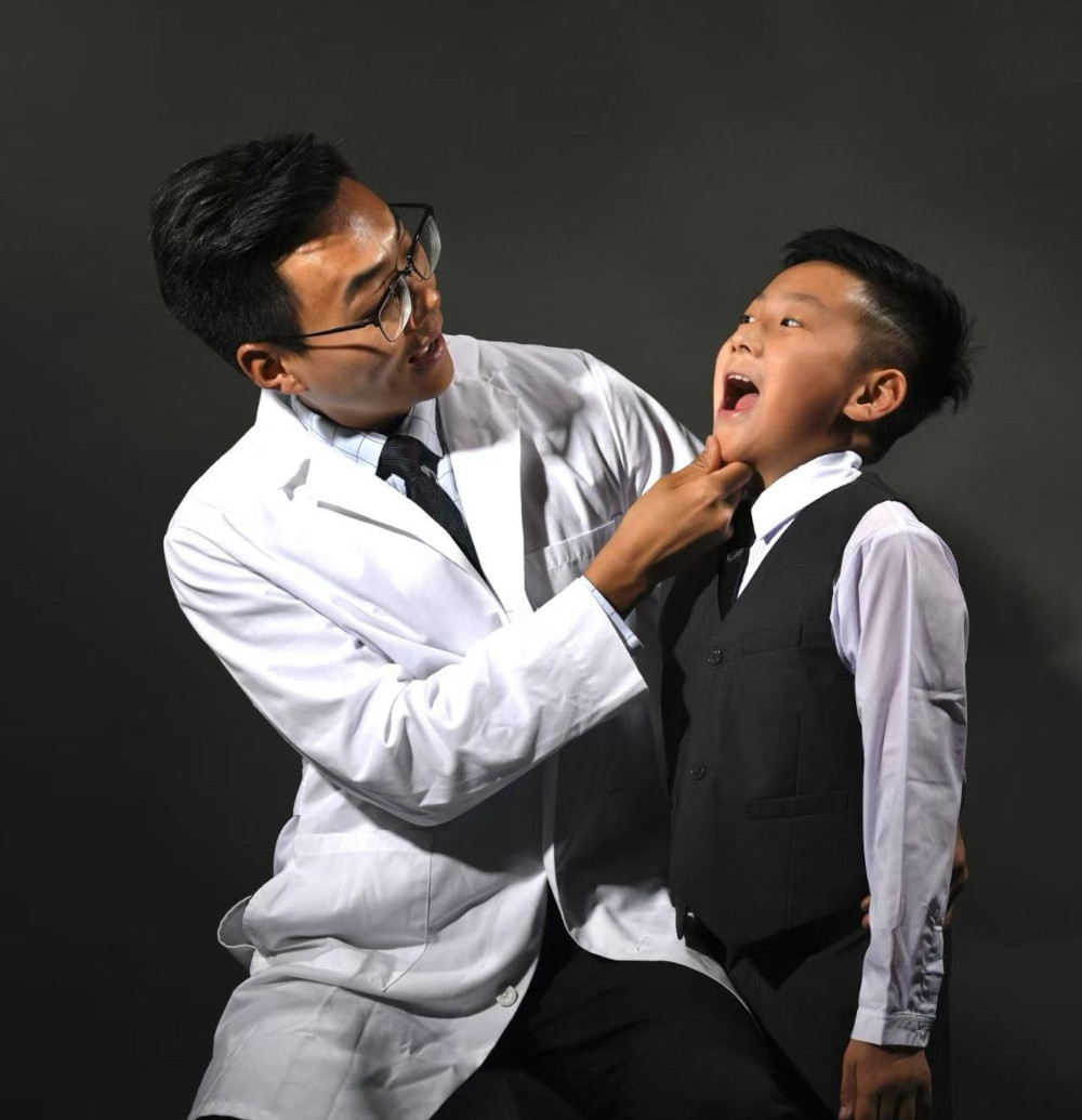 Dr. Lu treats a young patient - PhD Orthodontics Dr. Lu, in a white doctor's coat and black tie, inspects the mouth of a young patient - PhD Orthodontics