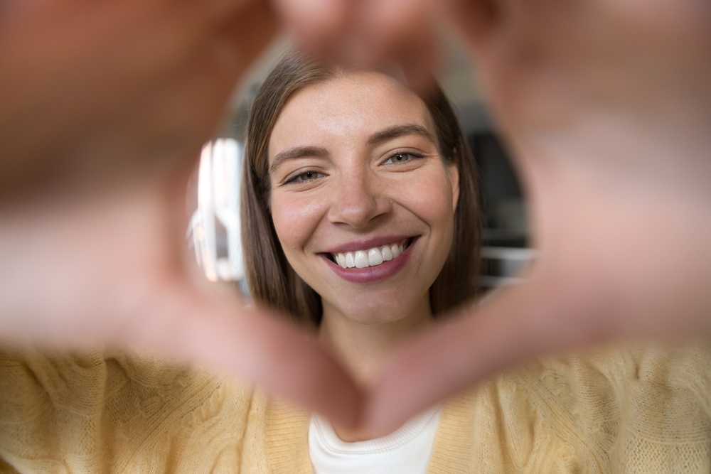 A joyful woman forms a heart shape with her hands around her radiant smile, showcasing the results of Invisalign treatment – Arcadia Invisalign