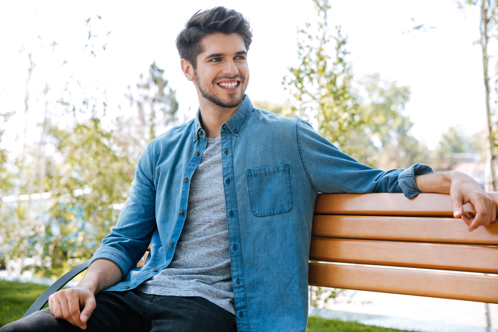 A young man relaxes on a park bench with a bright, confident smile, reflecting the natural results achievable with Invisalign treatment – Invisalign in Pasadena.
