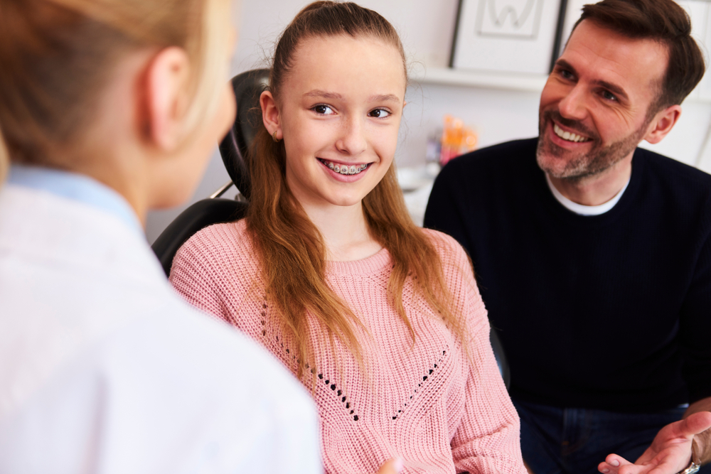 Teen Smiling with Braces During Consultation – Orthodontist in South Pasadena A teenage girl with braces smiles during her orthodontic appointment as her parent and doctor discuss her treatment progress – Orthodontist in South Pasadena.