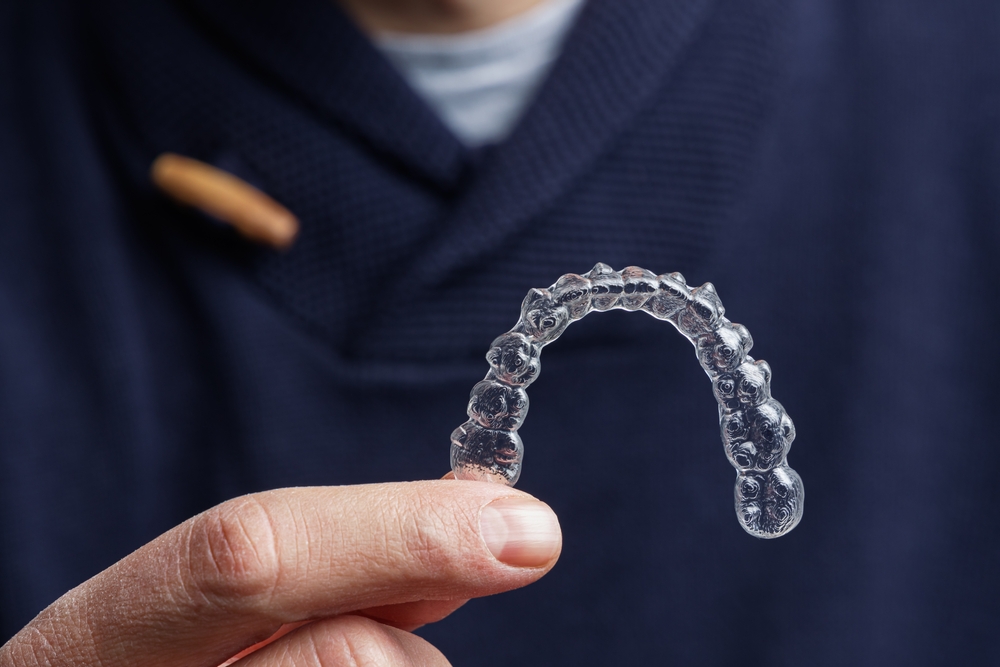 A detailed close-up of a person holding a clear Invisalign aligner, showcasing its slim, discreet design for comfortable orthodontic treatment – Invisalign in San Gabriel