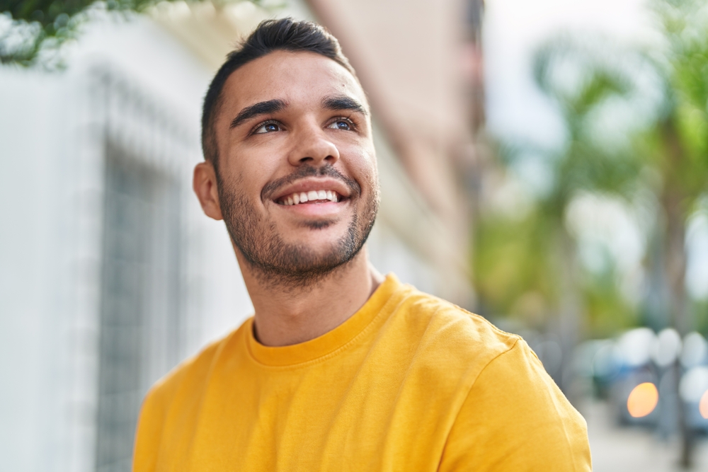 A young man smiles brightly outdoors, showing off his well-aligned teeth and the confidence gained from Invisalign – Invisalign in San Gabriel.