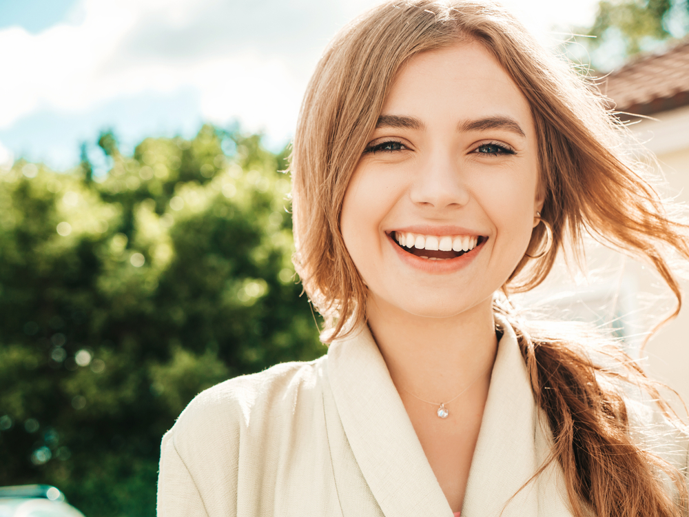 A cheerful woman smiles confidently outdoors, showing off beautifully aligned teeth achieved through Invisalign treatment – Invisalign Alhambra.