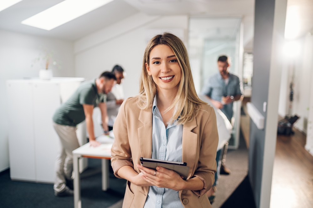 Confident Woman Smiling in Office Setting – Orthodontist in South Pasadena A young professional woman smiles warmly in an office environment, showcasing a healthy, confident smile achieved through quality orthodontic care – Orthodontist in South Pasadena.