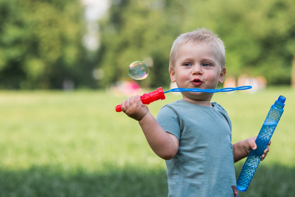 A young child blowing bubbles outdoors, holding a bubble wand and bottle with a look of delight - PhD Orthodontics A young child blowing bubbles outdoors, holding a bubble wand and bottle with a look of delight - PhD Orthodontics